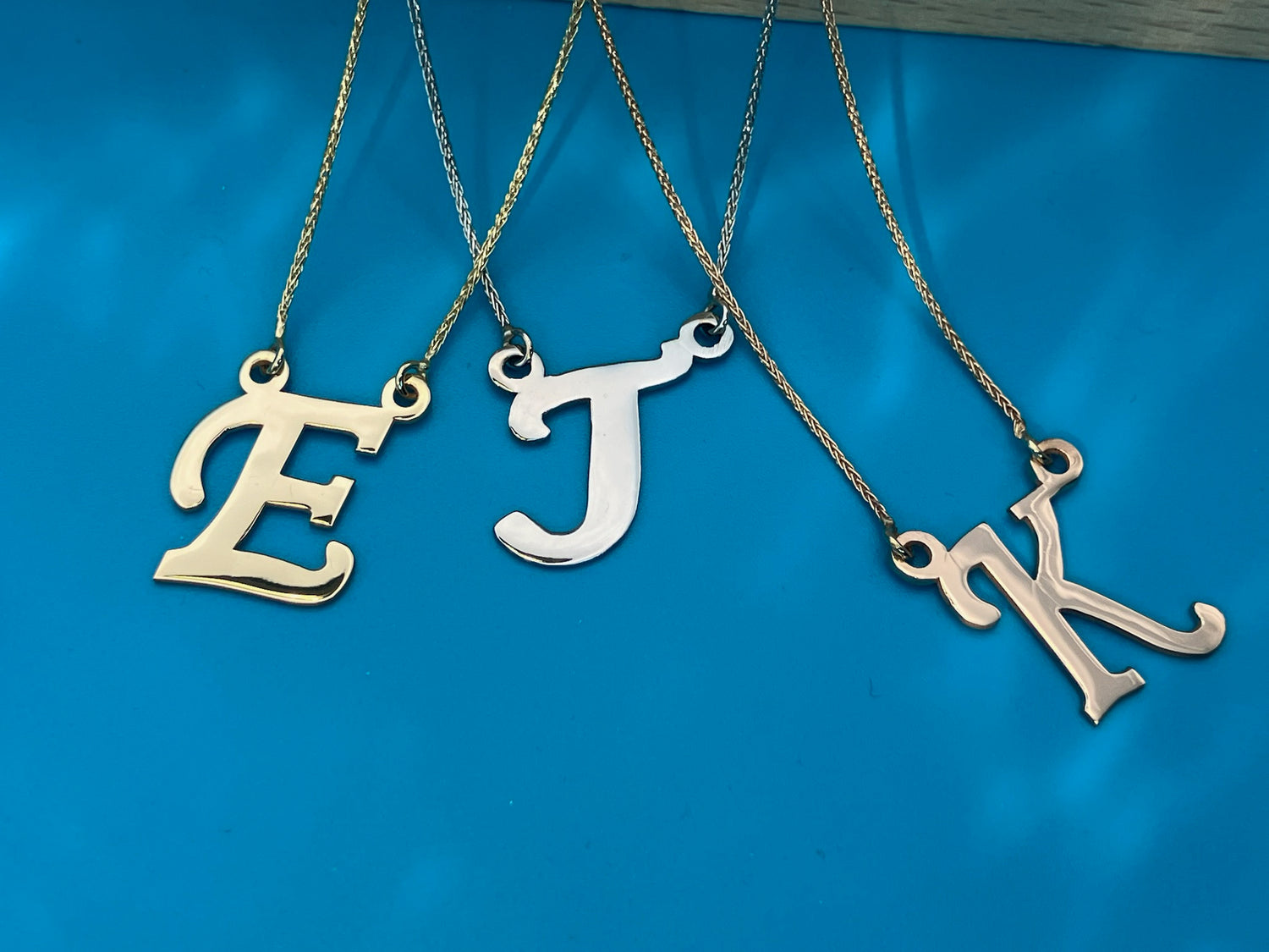 Our banner: 3 gold hue necklaces on watery blue background: Yellow 'E', white 'J', and rose 'K'.